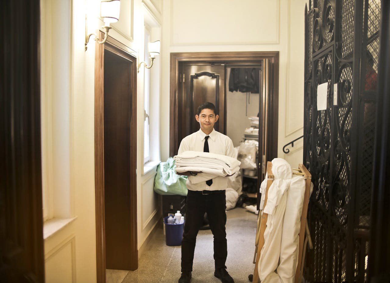 services-02 Professional hotel staff member carrying fresh linens in an elegant hallway.
